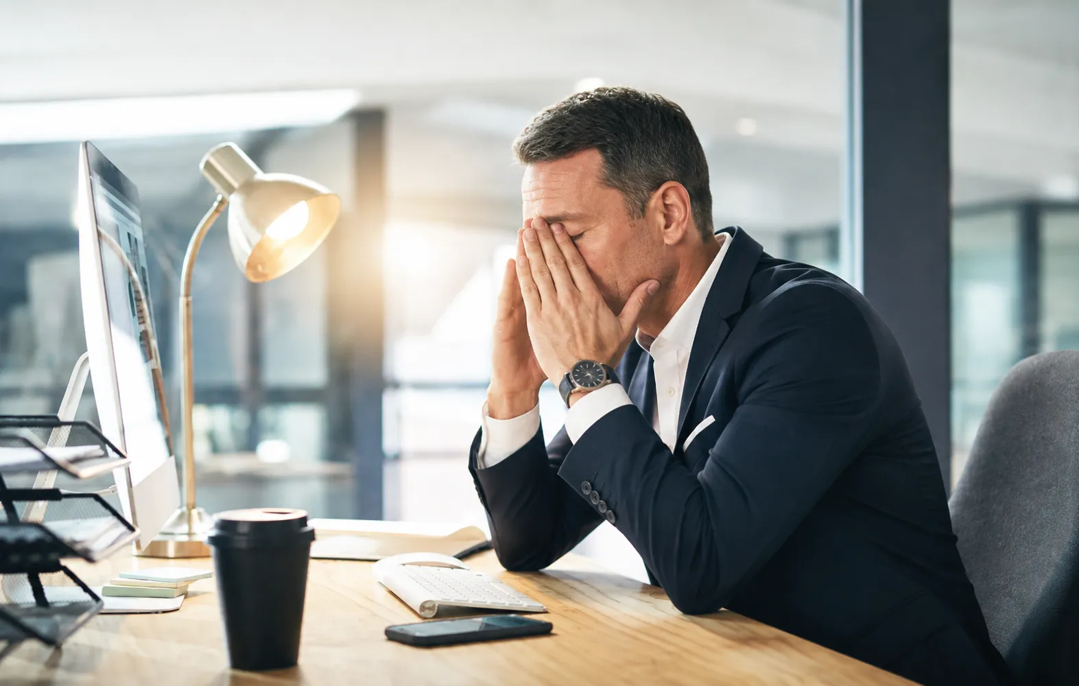 Homme d’affaires devant un écran d'ordinateur, soulageant sa fatigue oculaire en se tenant des deux mains l'arrête du nez
